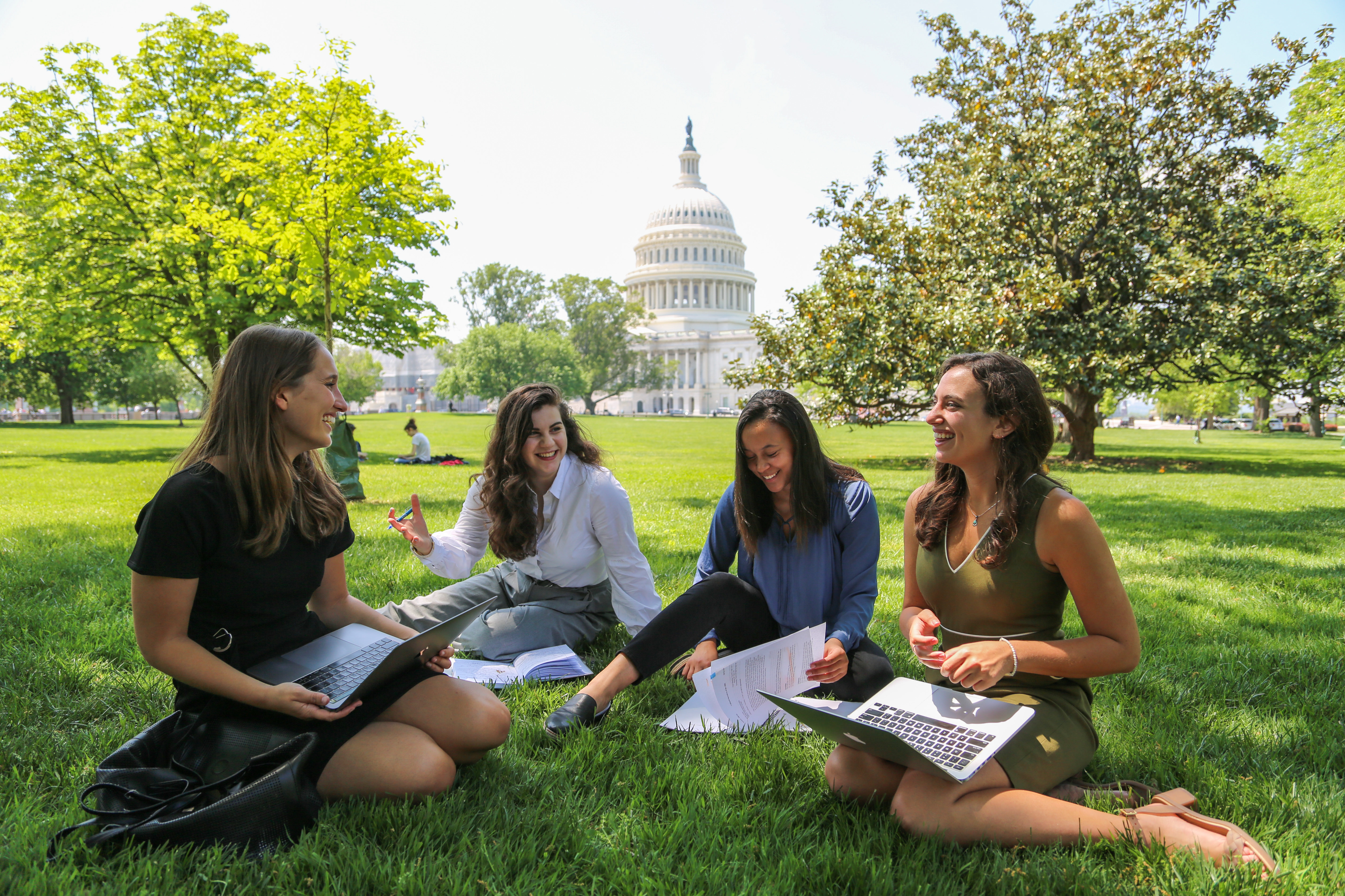 Four women sitting on the grass in front of the Capitol Building